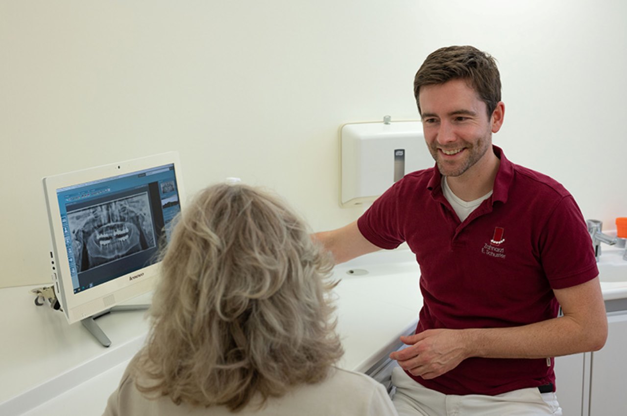 Zahnarzt Eric Schuster zeigt auf dem Computer das Orthopantomogramm der Patientin - Vollkeramische Kronen 
